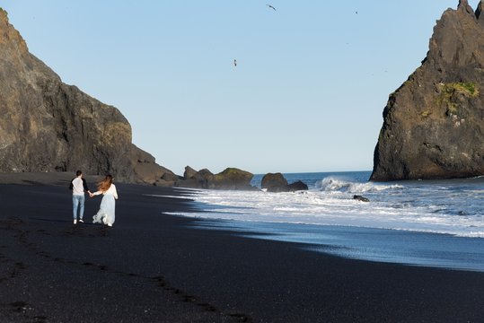 Male + Female Couple walking on a black sand beach in Iceland 
