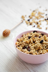 Pink bowl of fruit granola and honey, side view.
