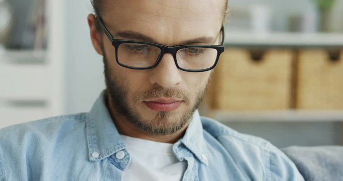 Close up of the handsome man's face in glasses looking serious and thoughtful while man using some device. Portrait. Inside.