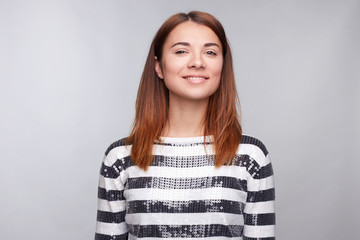 Fototapeta premium Pretty smiling joyfully female with fair hair, dressed casually, looking with satisfaction at camera, being happy. Studio shot of good-looking beautiful woman isolated against blank grey studio wall.