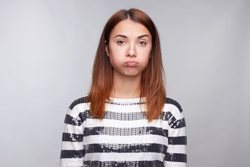 Fototapeta premium Offended upset young stylish female blowing cheeks, has grumpy expression, poses against white background, being unsatisfied and disappointed after conflict with teacher or colleagues, makes grimace.