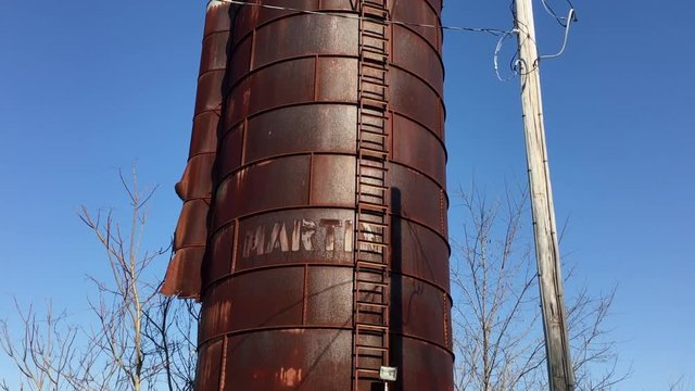 Rusty old grain silo lies derelict and abandoned on farm land.
