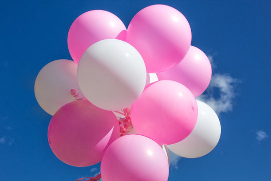 Balloons, pink and white on a background of blue sky with clouds.