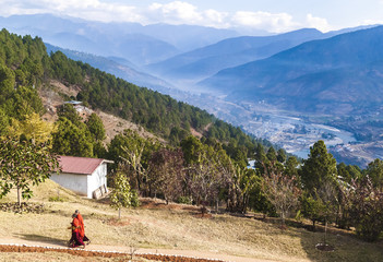 Two Buddhist monks in their traditional red clothes on the territory of women Buddhist Monastery in Bhutan, Punakha valley on the background.. © sunday_morning
