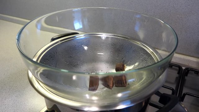 Dropping chocolate cubes into bowl, water bath, steam.