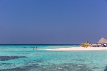 Maldives, Feb 8th 2018 - Tourists swimming in a turquoise blue sea, desert island, small traditional hut hotel on a blue sky day, paradise feeling in Maldives.