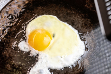 An egg frying in butter and oil in a carbon steel skillet