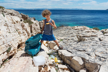 Little boy cleaning up beach full of rigid plastic bottles and other garbage washed out on coast.