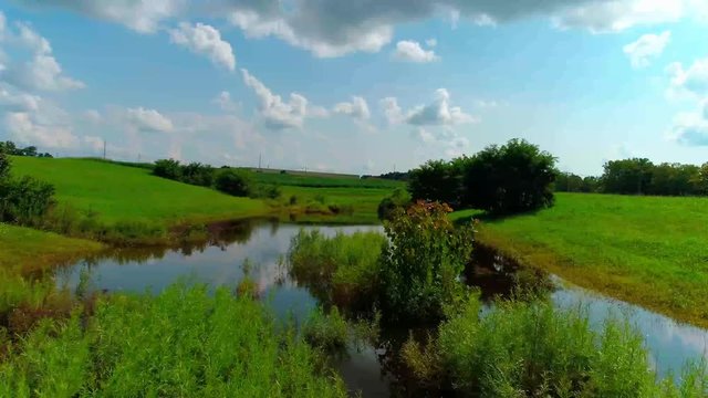 Flying over a pond on a farm blue skies and clouds reflecting off the surface of the water