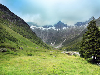 Fototapeta na wymiar Susten Pass in Switzerland. High Alps and valley of green grass. Bad weather on the way. Clouds resting on the top of the mountains.