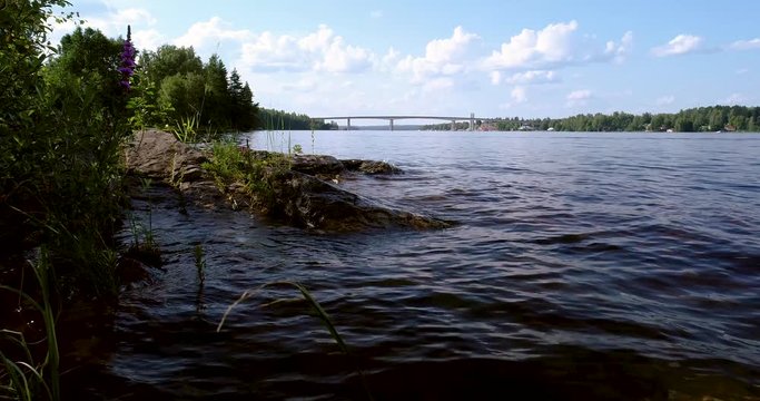 Waves on the beach and cliff by the lake and a big birdge in the background on a summer day, Puumala Finland