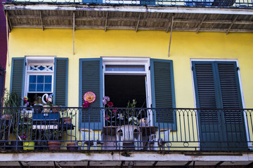 Yellow Colonial House with Green Shutters and a Balcony Filled with Eclectic Decorations in the...
