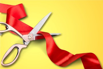 Scissors cutting red ribbon, close-up view on blue background