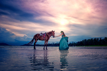 Nice lady in green dress walking on the beach with horse