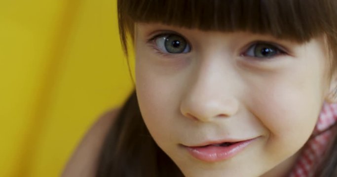Close up of the cute little girl blinking to the camera and smiling while sitting on the yellow sofa.