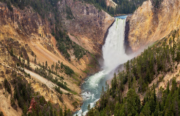 The Grand Canyon waterfall of Yellowstone roaring over a mountain edge viewed from the top of a hill in a summertime afternoon landscape