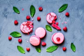 flatlay food items: macaroon cakes pink color, fresh raspberries and green mint leaves lying on gray concrete backgroubd
