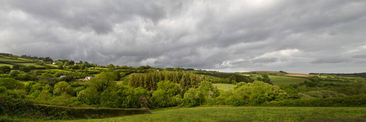 Fototapeta na wymiar Panorama of British Countryside with trees and fields under a stormy sky