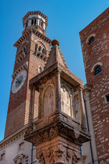 Obraz premium Ancient column on Erbe square in Verona. On the column there is the coat of arms of the Visconti family and a relief image of the figures of the saints. In the background is the Lamberti tower
