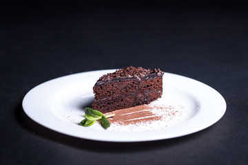 Fototapeta na wymiar Delicious chocolate cake on a white plate. Isolated on a dark background.