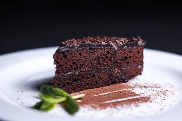 Delicious chocolate cake on a white plate, on a dark background.