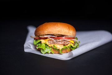 Burger with a chop on a parchment on a black background