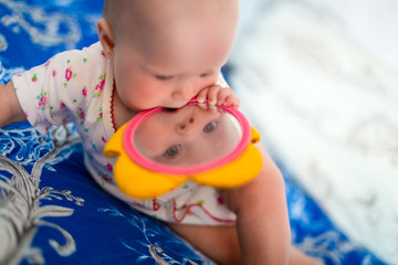 Adorable and cute baby girl sits on the bed and plays with toys that is children mirror. Small...