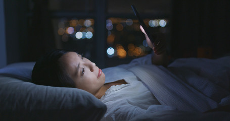 Woman use of mobile phone and lying on bed at night