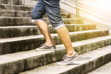 Young man in blue jeans and sneaker shoes walking up stairs outdoors background with copy space for text. Concept of person's lifestyle.
