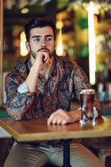 Thoughtful bearded man wearing casual clothes sitting in a modern pub.
