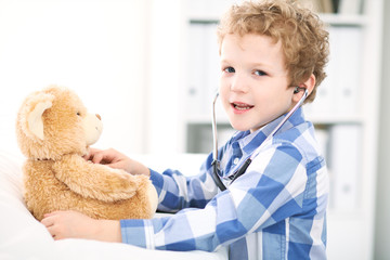 Child  patient afrer health exam playing as a doctor with stethoscope and teddy bear