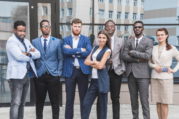 Successful company with happy workers. Men and women in business suits stand with their arms crossed against the background of skyscrapers