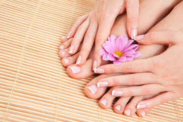 Obraz na płótnie Canvas Care for beautiful woman skin and nails. Pedicure and manicure at beauty salon. Woman legs, hands with flower on bamboo. Spa therapy. Closeup photo of female feet with white french manicure, pedicure