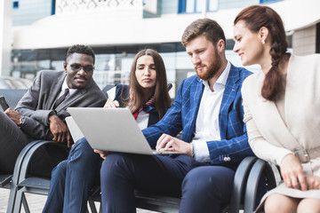 Group of happy diverse male and female business people team in formal gathered around laptop computer in bright office against the background of a glass building