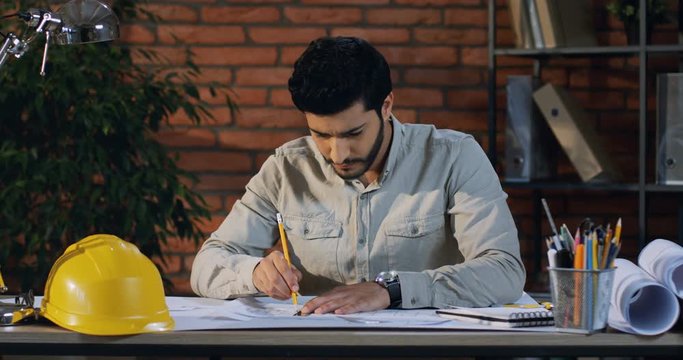 Young man constructor ot architect sitting at the desk in the office and working over the new project drawings.