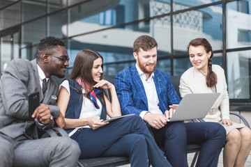 Group of happy diverse male and female business people team in formal gathered around laptop computer in bright office against the background of a glass building