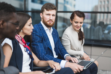 Group of happy diverse male and female business people team in formal gathered around laptop computer in bright office against the background of a glass building