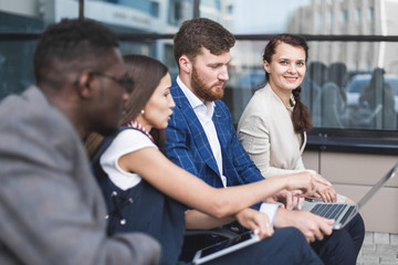 Group of happy diverse male and female business people team in formal gathered around laptop computer in bright office against the background of a glass building