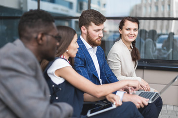 Group of happy diverse male and female business people team in formal gathered around laptop computer in bright office against the background of a glass building