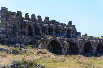 ruins of an ancient city wall with arched niches on the background of clear blue sky