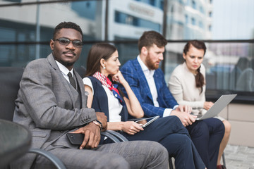 Group of happy diverse male and female business people team in formal gathered around laptop computer in bright office against the background of a glass building