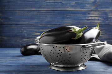Colander with raw ripe eggplants on table