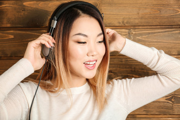 Portrait of happy Asian woman listening to music against wooden background