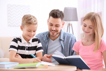 Cute little boy doing homework with father and sister