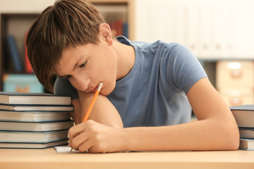 Tired teenager boy doing homework in library