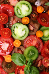 various colorful tomatoes and basil leaves on rustic table.
