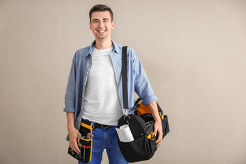 Young plumber with tool belt and bag on light background