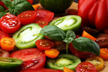 various colorful tomatoes and basil leaves on rustic table.