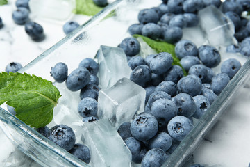 Juicy blueberries with green leaves and ice on table, closeup