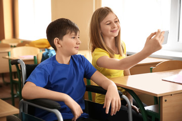 Teenage girl with boy in wheelchair taking selfie at school